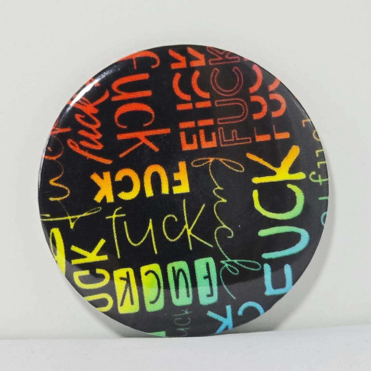 Round button badge with colorful 'FUCK' text on a black background