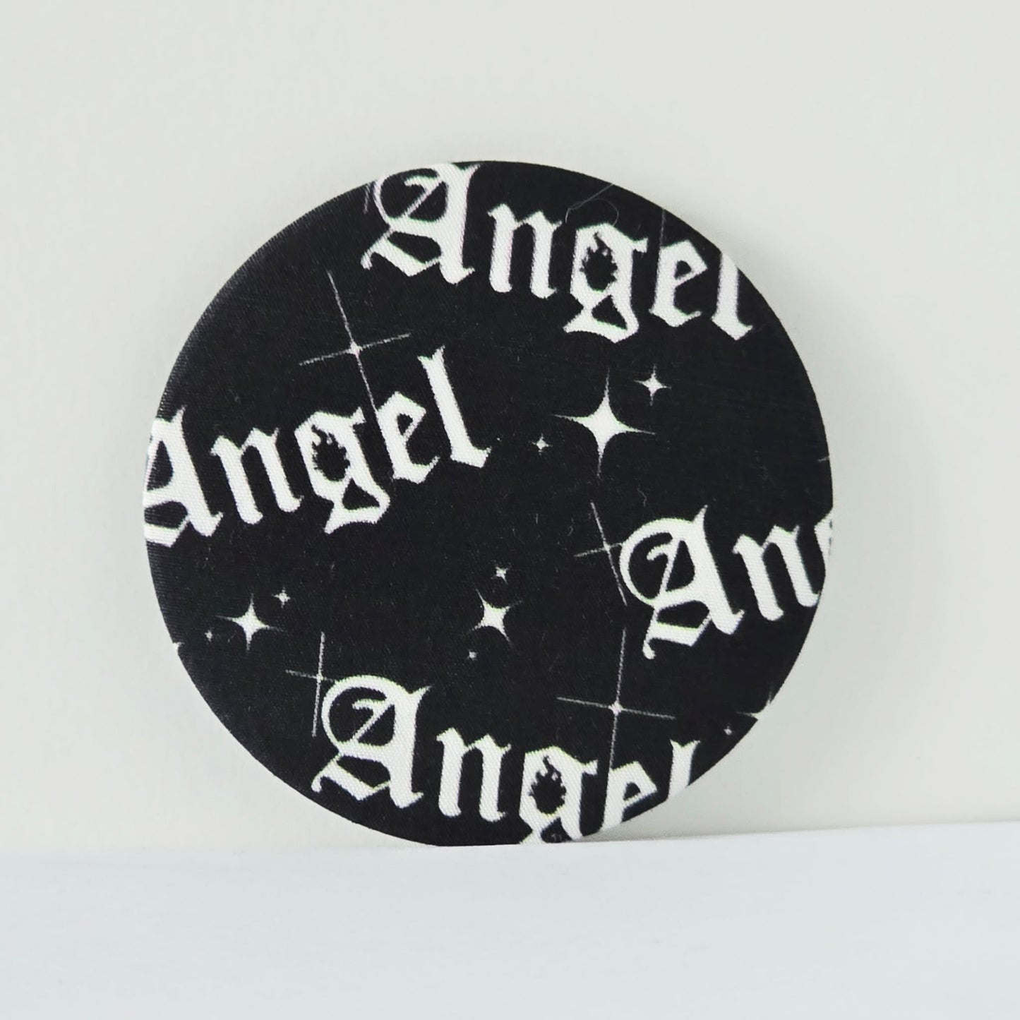 Circular black coaster with 'Angel' text and star patterns on a white background