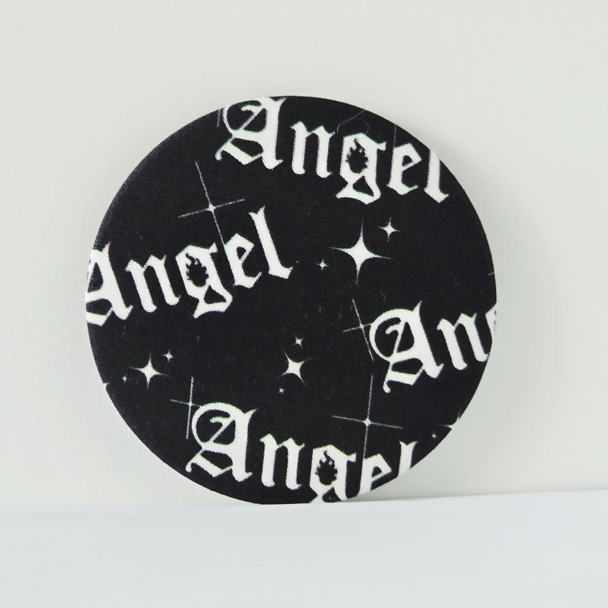 Circular black coaster with 'Angel' text and star patterns on a white background