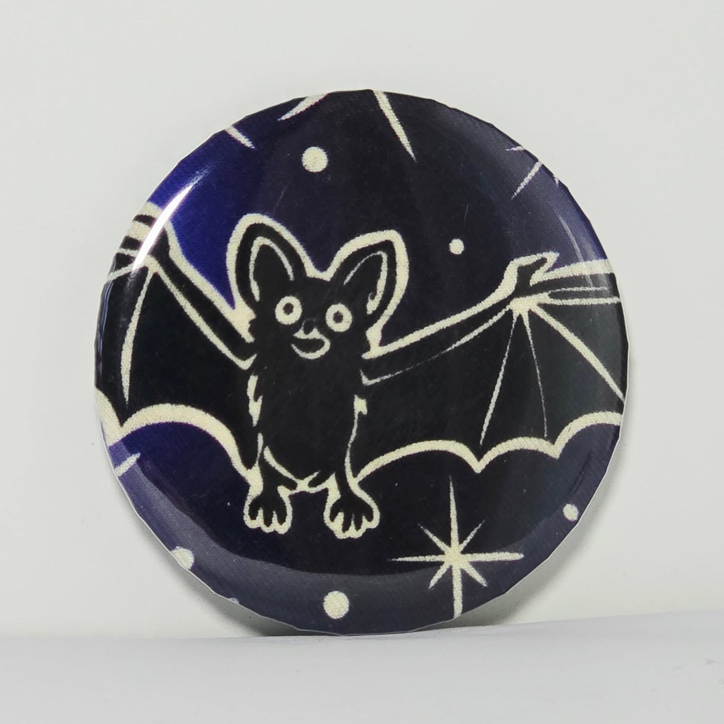 Round black magnet with white bat design on a blue background