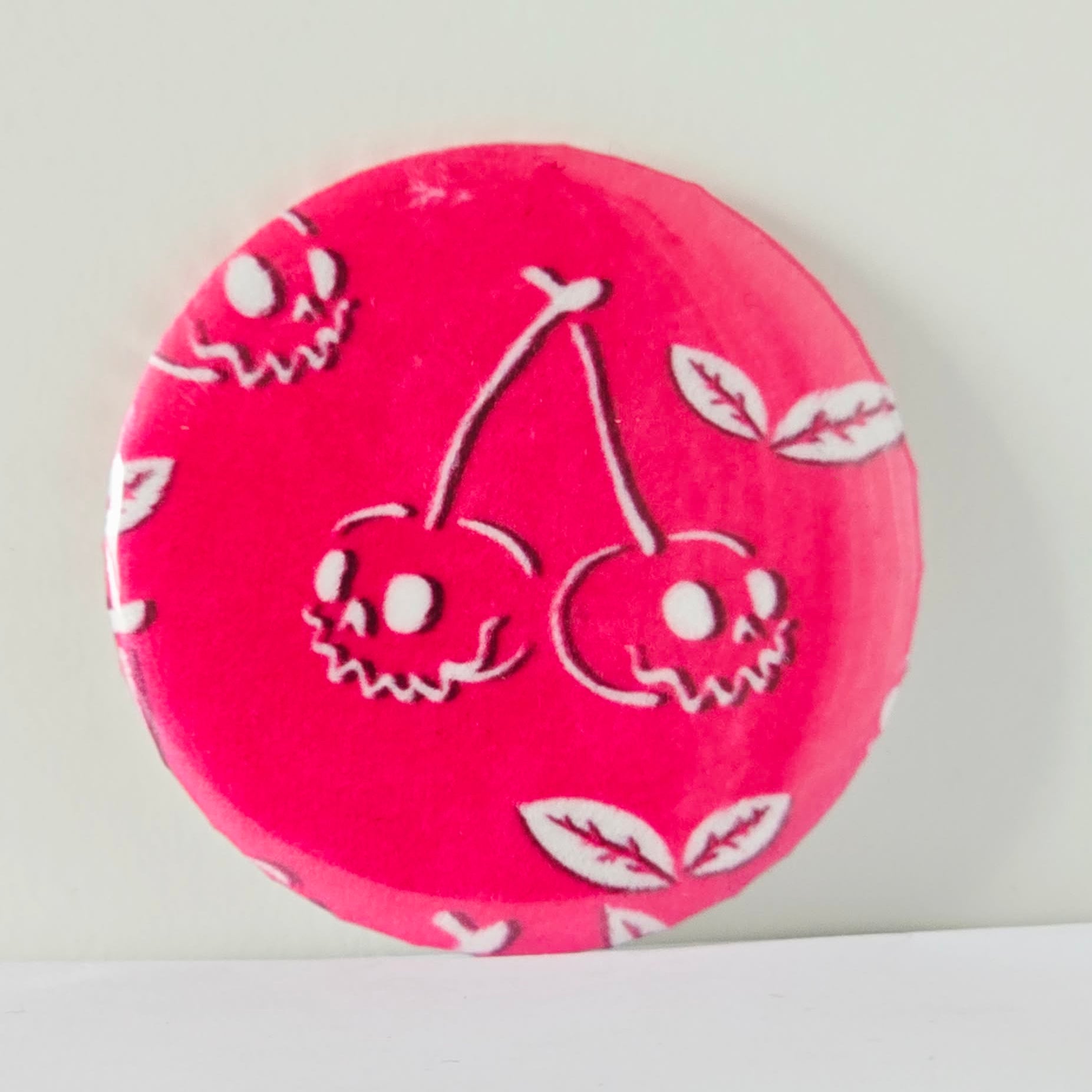 Pink round object with white skull and cherry design on a light gray background
