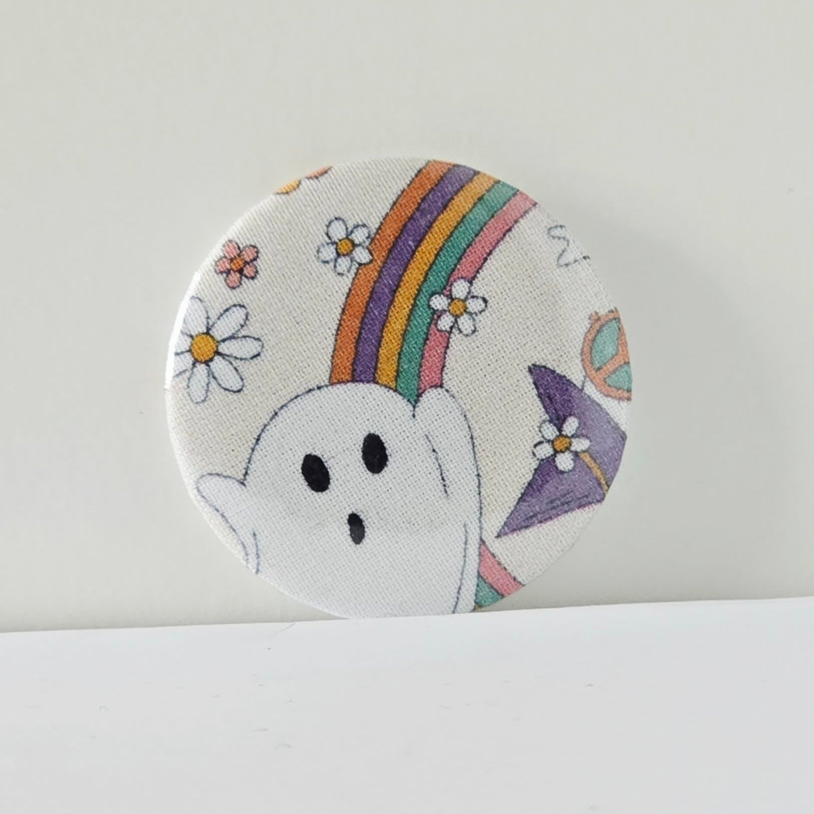 Circular patch with a ghost, rainbow, and flowers on a white background